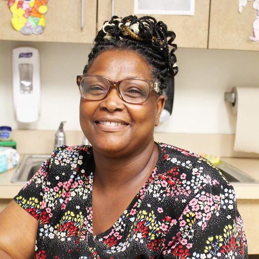A woman in floral nurse scrubs smiling at the camera